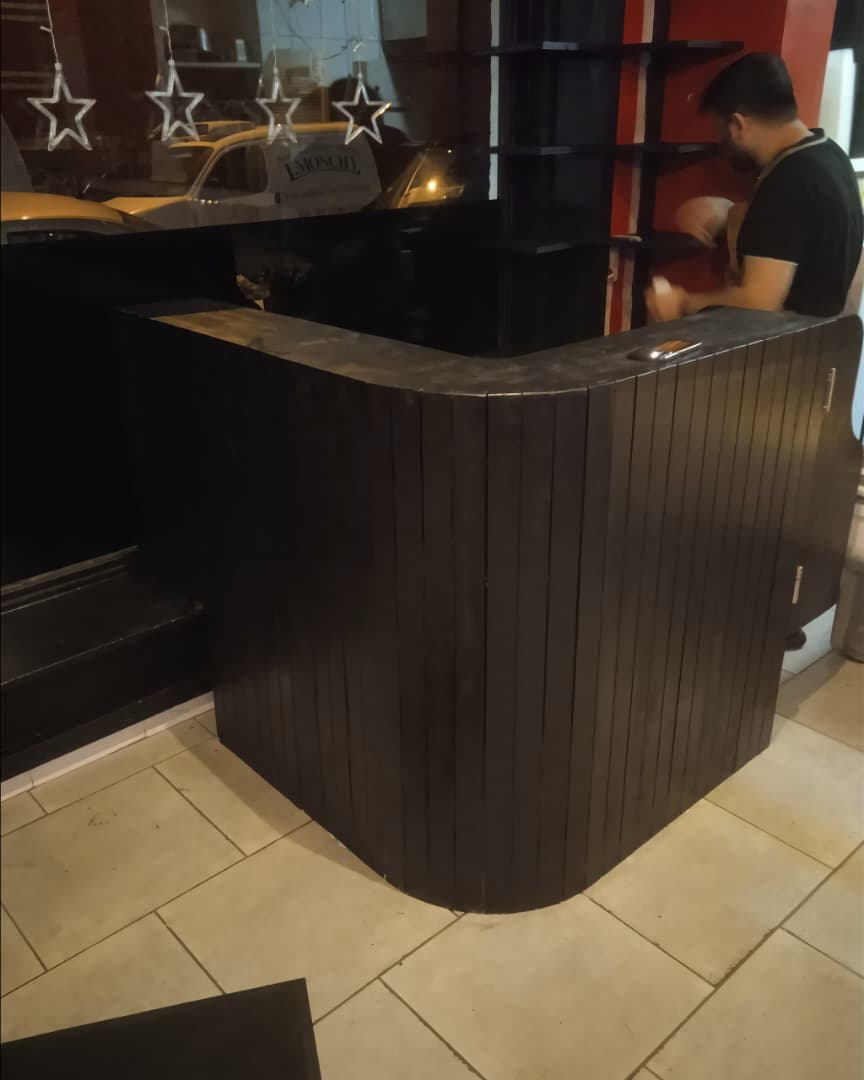 Un comptoir de bar d'angle (ou meuble de réception d'angle) en bois noir ou sombre.