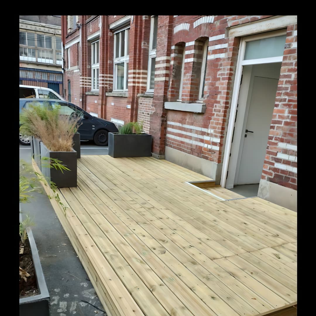 Une terrasse en bois (ou un plancher / deck en lattes de bois) installée à l'extérieur le long d'un bâtiment en briques.