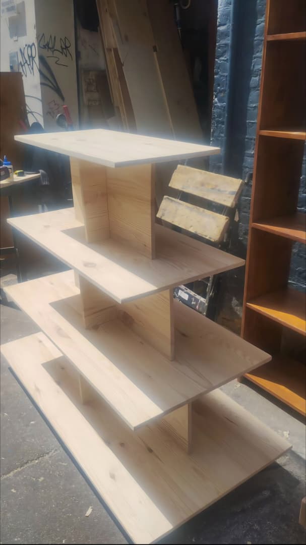 présentoir central à étages en bois clair (généralement utilisé en boutique pour exposer des produits), avec une structure pyramidale ou en escalier.