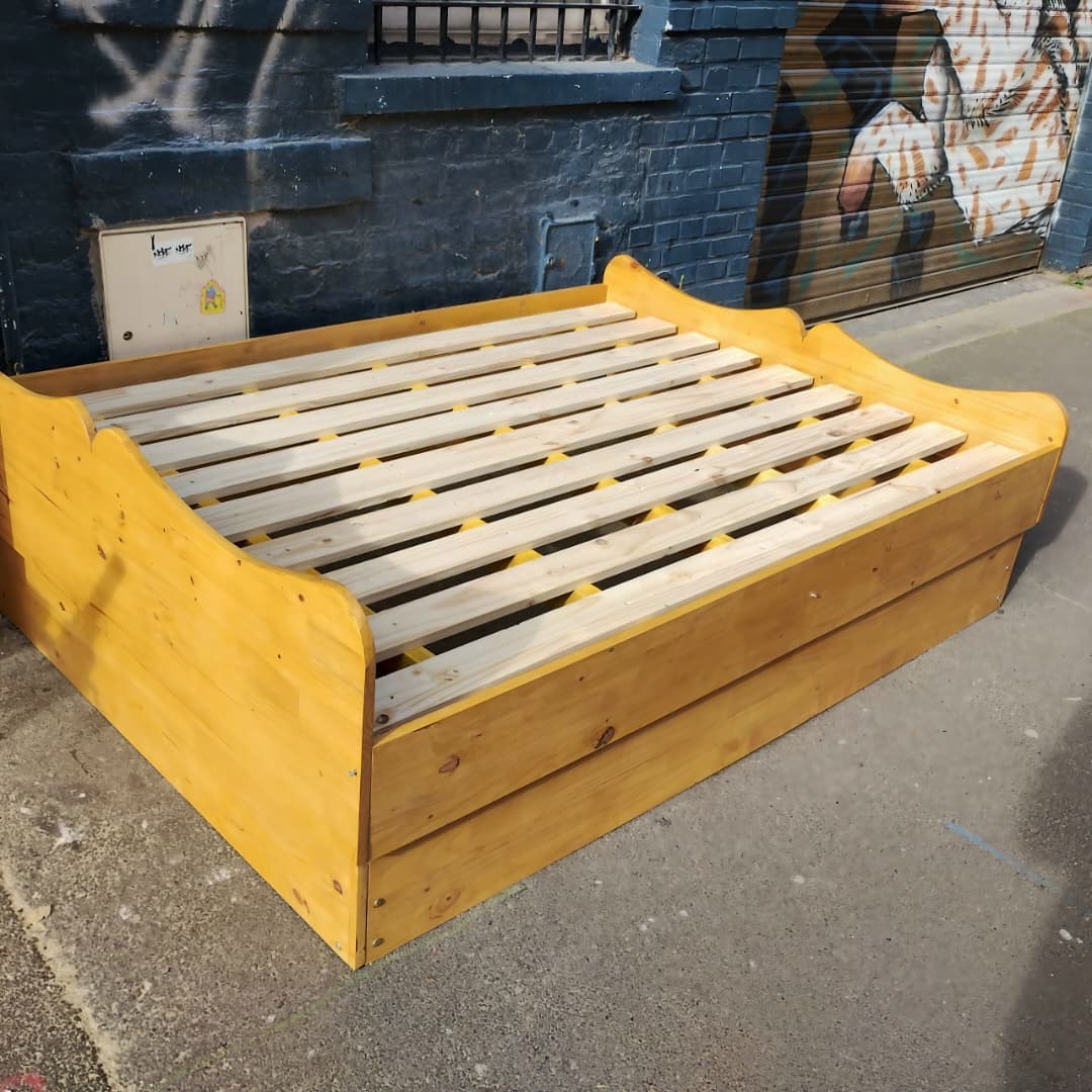 Un cadre ou sommier de lit en bois massif avec un sommier à lattes apparentes (probablement un lit banquette ou un lit gigogne).
