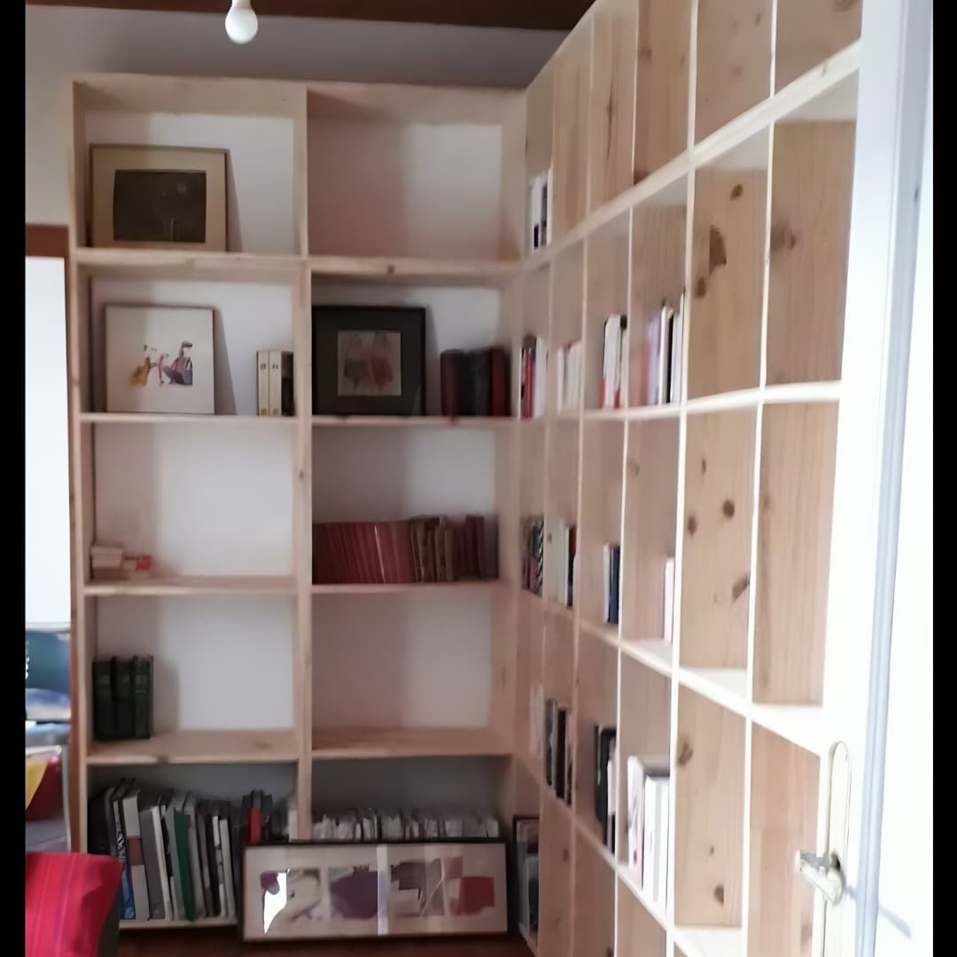 Une vue d'ensemble d'une grande bibliothèque d'angle à cases en bois clair, installée dans une pièce et servant à ranger des livres et des cadres de décoration.